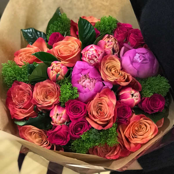 Bouquet of pink and peach roses with green filler wrapped in brown paper