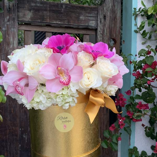 Pink orchids and white roses in a gold hatbox with a ribbon