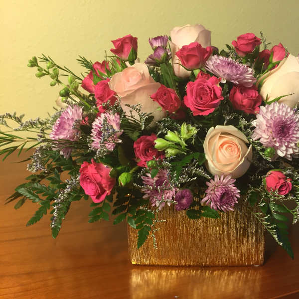 Bouquet of pink and white roses with purple daisies in a gold vase