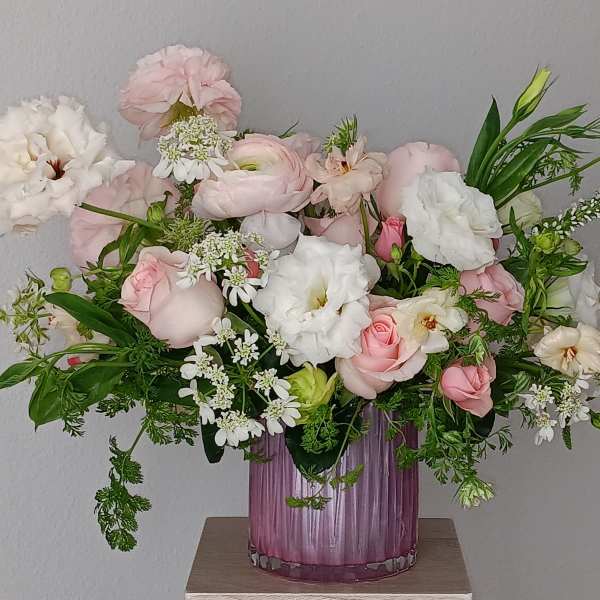Pink and white flower arrangement in a purple glass vase