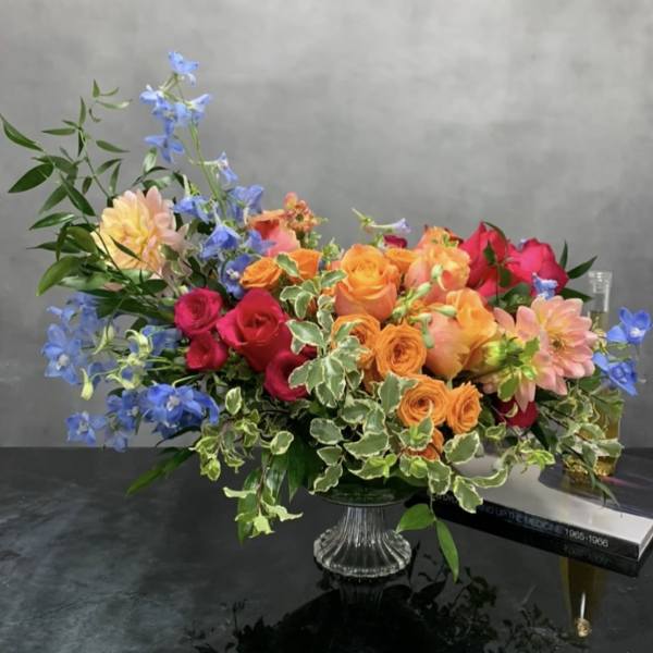 Colorful mixed bouquet in a clear glass vase with blue flowers and roses