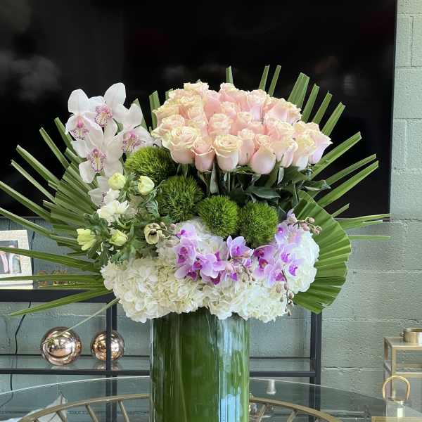 Large pastel floral arrangement in a glass vase with roses, orchids, and hydrangeas
