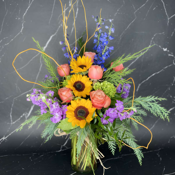 Bouquet of sunflowers, pink roses, and purple flowers in a glass vase