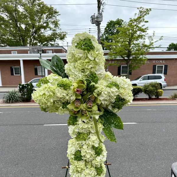 Large floral cross on an easel with pale green and white blooms
