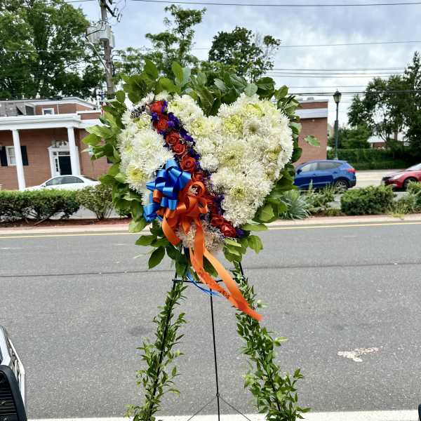 Heart-shaped floral standing spray with white flowers, red roses, and blue-orange ribbons