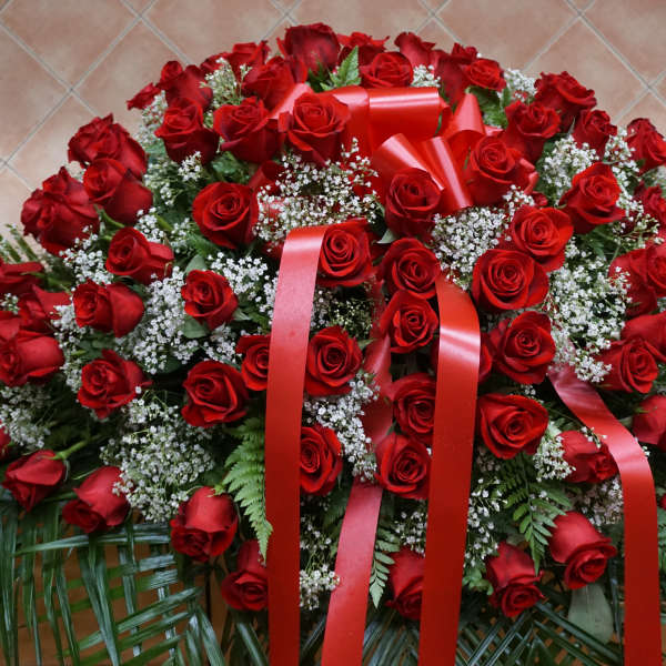 Large arrangement of red roses with white filler flowers and red ribbons