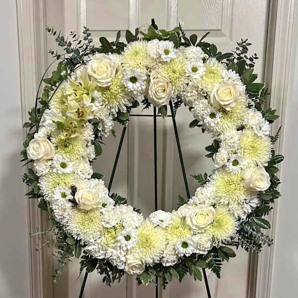 White floral wreath on a black stand with roses and mums