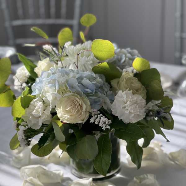White and pale blue floral centerpiece in a glass vase