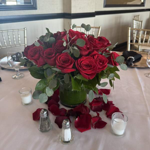 Red rose centerpiece in a glass vase with scattered petals