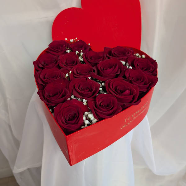 Heart-shaped red box filled with deep red roses and small white filler flowers