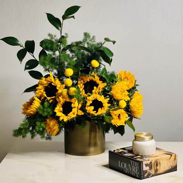 Sunflower arrangement in a gold vase with green foliage