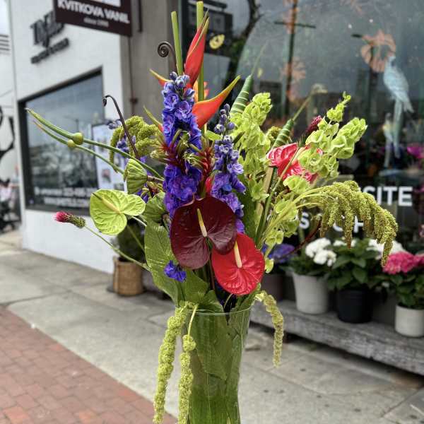 Tall tropical arrangement in a glass vase with red anthuriums and purple flowers