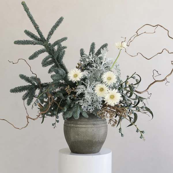 White daisy-like flowers in a gray vase with evergreen branches