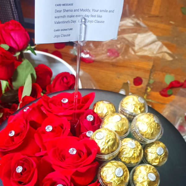 Red roses arranged with gold-wrapped chocolates in a heart-shaped box