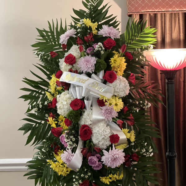 Standing funeral wreath with red, pink, yellow, and white flowers