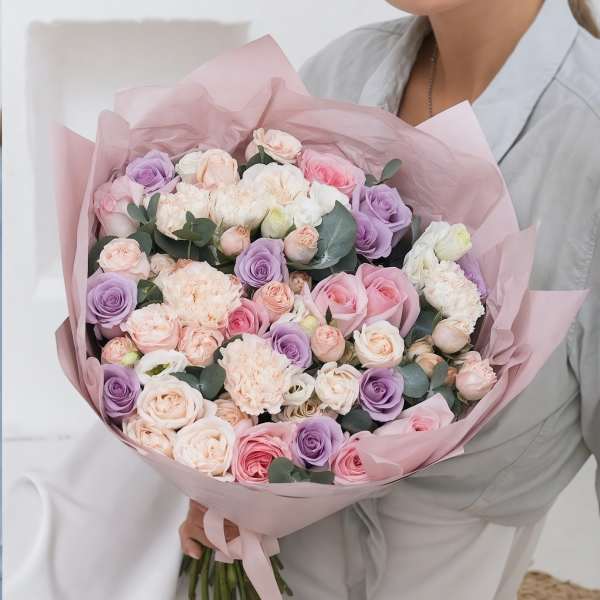 Large bouquet of pink, lavender, and cream roses wrapped in blush paper