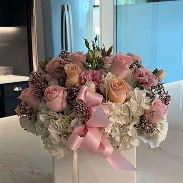 Pink and peach roses with white hydrangeas in a white box, tied with a pink ribbon
