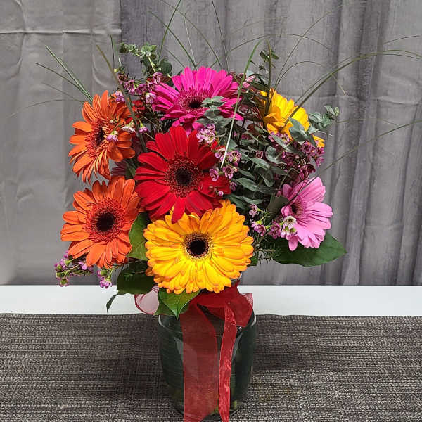 Colorful gerbera daisy bouquet in a glass vase with a red ribbon