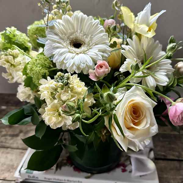 Bouquet of white daisies, cream roses, and pale green blooms in a black vase