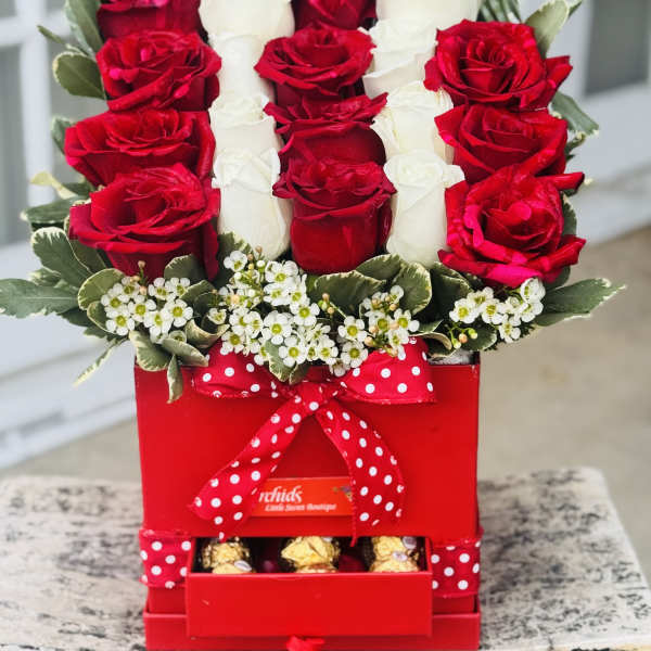 Red and white roses arranged in a red gift box with chocolates and a polka-dot ribbon
