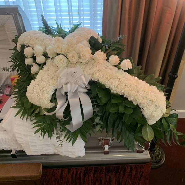 White roses and hydrangeas arranged on a casket with a white ribbon