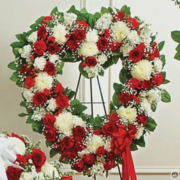 Heart-shaped wreath of red and white flowers on a stand with a red ribbon