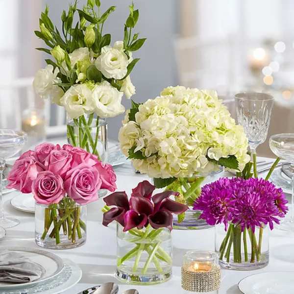 Four floral centerpieces in glass vases on a set table