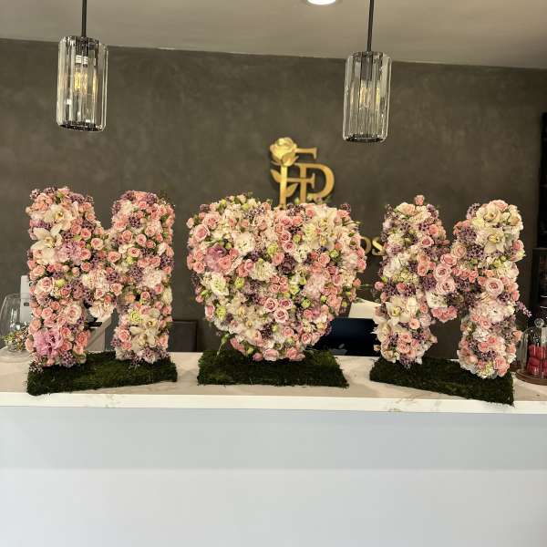 Large floral letter arrangements in pink, white, and lavender on moss bases