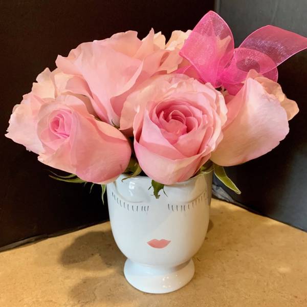 Pink roses arranged in a white face-shaped vase with a pink bow