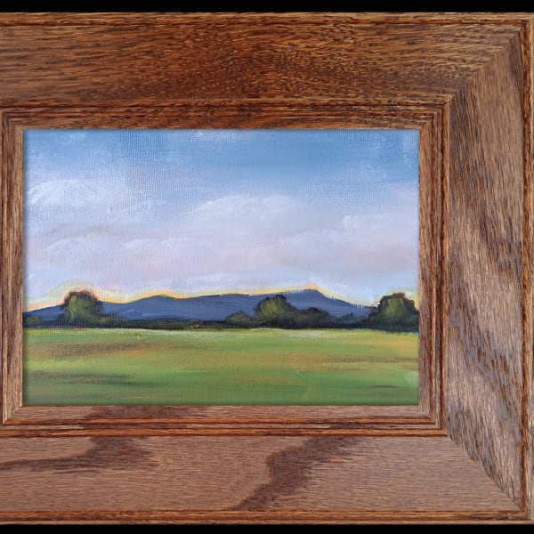Framed landscape painting of a grassy field and distant hills