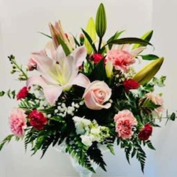 Pink lilies and roses arranged in a clear glass vase