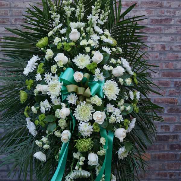 White floral standing spray with teal ribbons against a brick wall