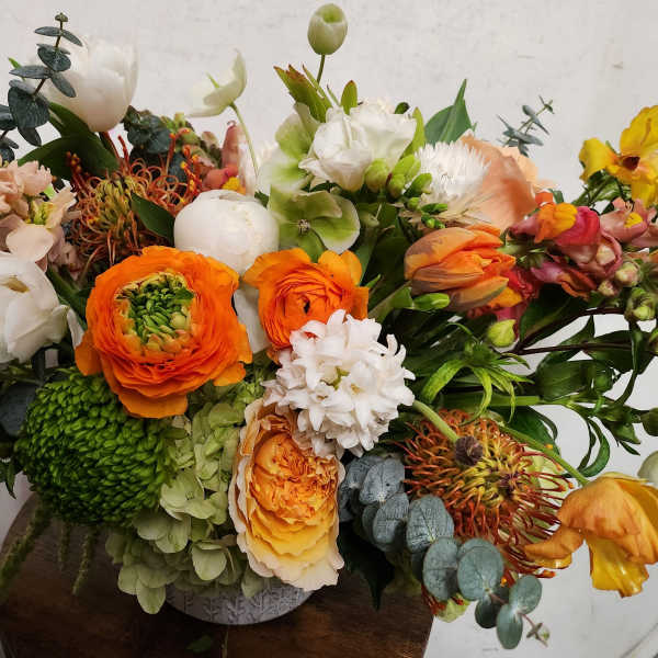 Colorful mixed flower arrangement in a low vase with orange, white, and green blooms