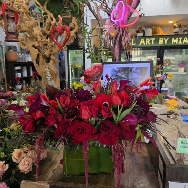 Red and burgundy floral arrangement in a green box with heart decorations