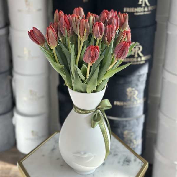 Red tulips arranged in a white vase with a ribbon