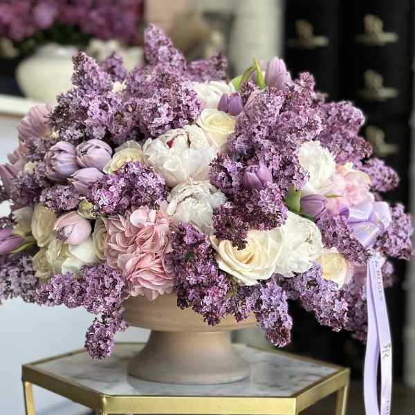 Lavender and white floral arrangement in a pedestal bowl with a ribbon