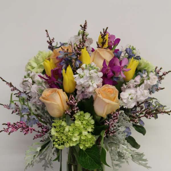 Mixed bouquet of roses, tulips, and purple orchids in a glass vase