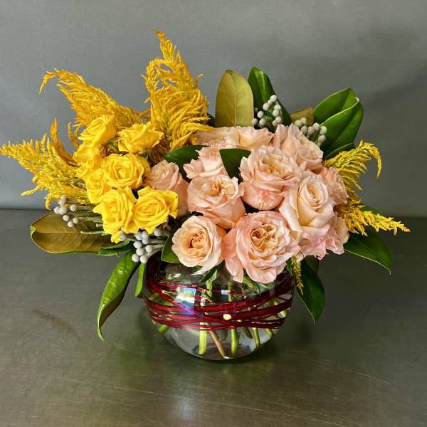 Pink and yellow roses arranged in a glass vase with red wrap