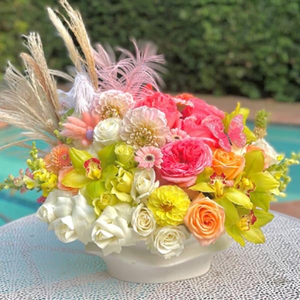 Colorful floral arrangement in a white bowl vase with feathers