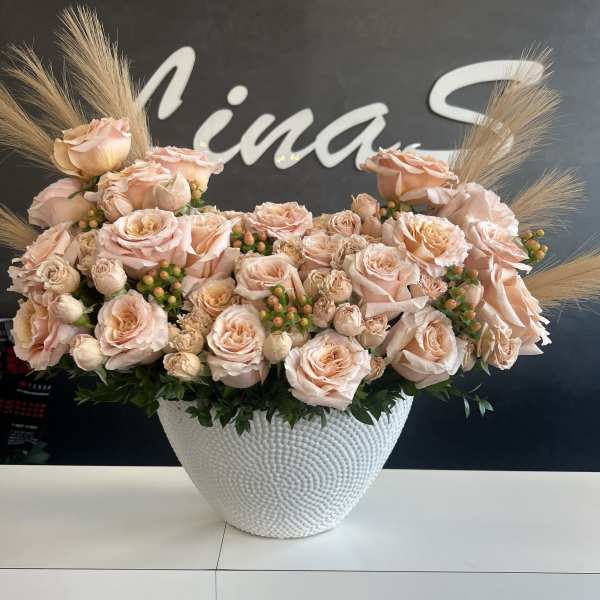 Peach rose arrangement in a white textured vase with dried grass accents