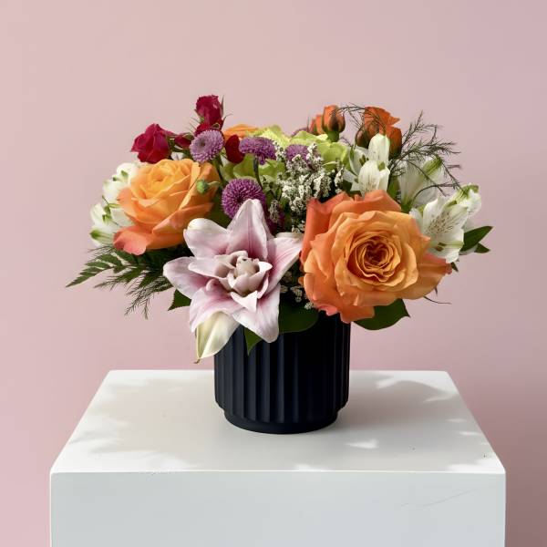 Mixed bouquet of roses, lilies, and purple blooms in a black vase