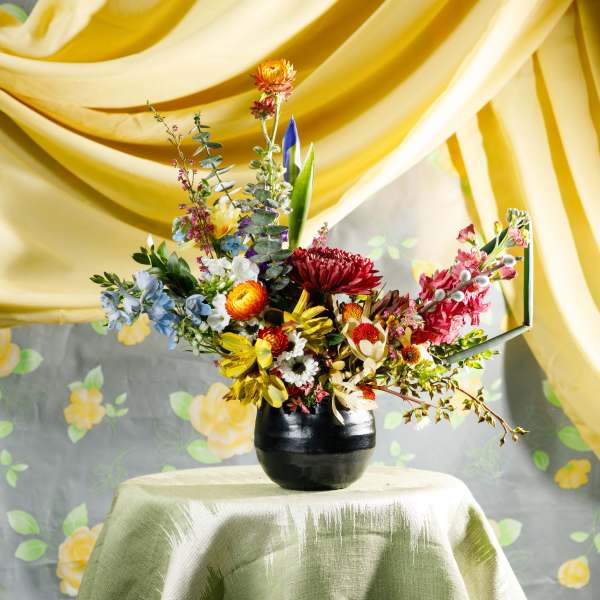 Colorful wildflower-style arrangement in a black vase on a draped table