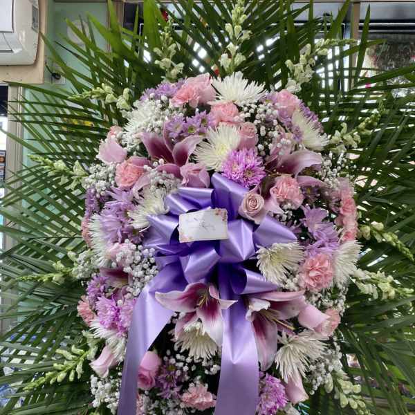 Large purple and pink funeral wreath with lilies and ribbon