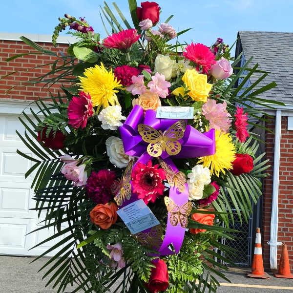Large standing floral spray with bright mixed flowers and purple ribbon