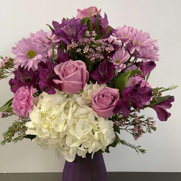 Pink and purple bouquet with roses, hydrangea, and daisies in a purple vase