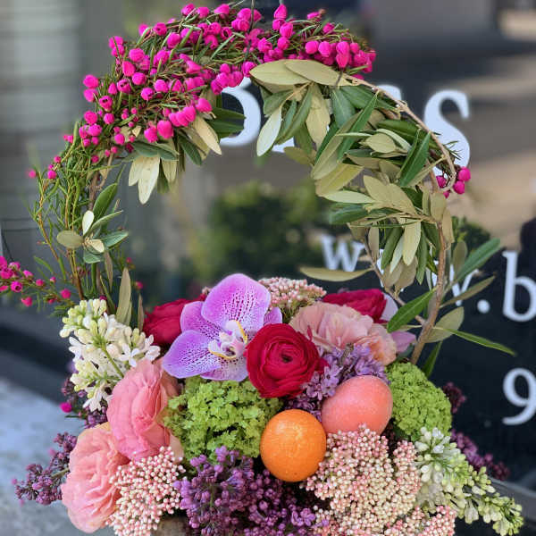 Pink and purple floral arrangement in a stone pot with a leafy wreath handle