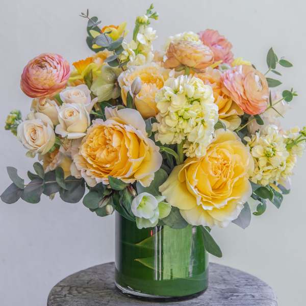 Yellow and peach roses in a green glass vase