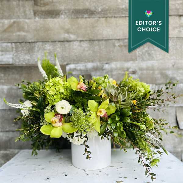 Green floral arrangement in a white vase with orchids and succulents