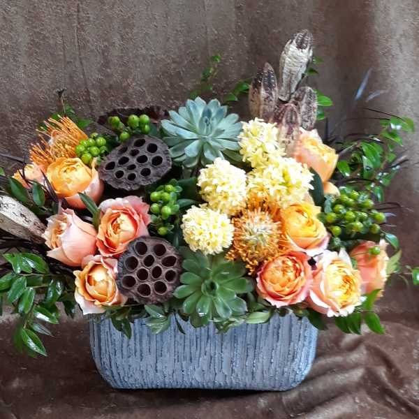 Arrangement of peach roses and pale yellow blooms in a textured gray container
