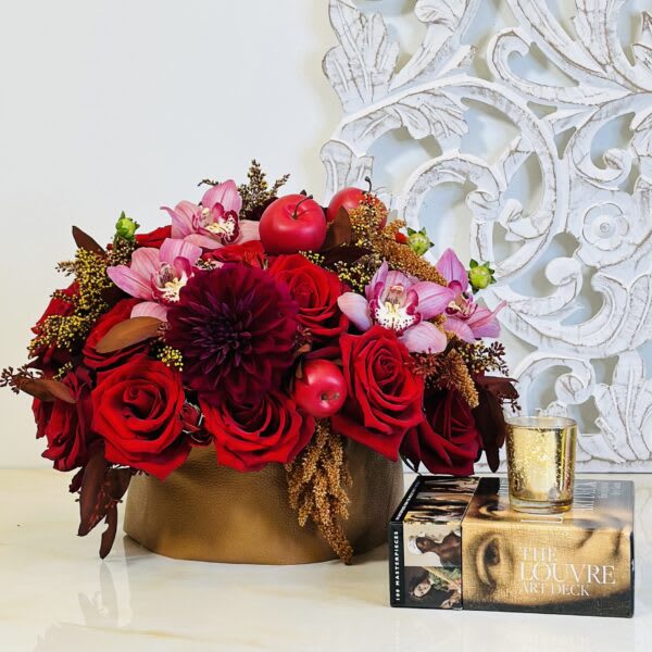 Red roses and pink orchids in a gold box with a candle beside it